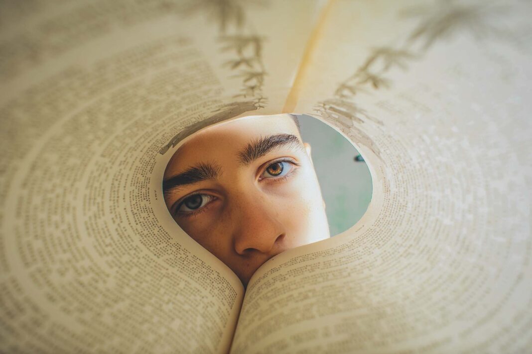 un adolescente che guarda attraverso un libro